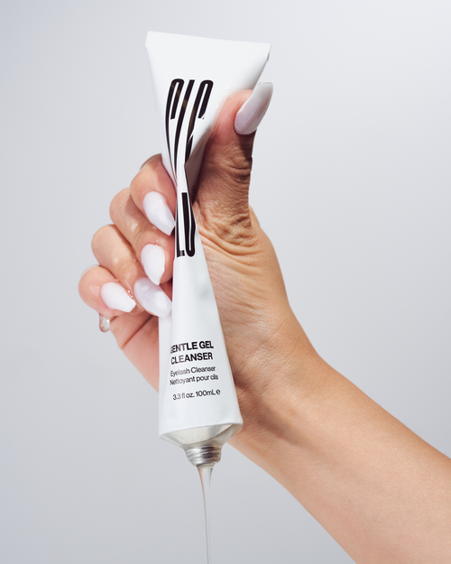 A model's hand squeezing a tube of Gentle Gel Cleanser for eyelash extensions.
