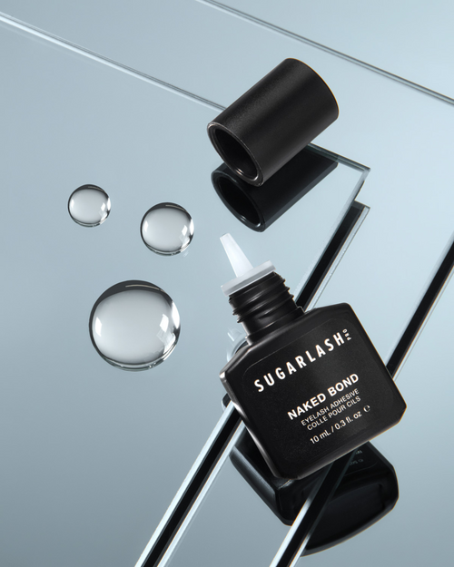 A bottle of Naked Bond eyelash glue with drops of lash glue by it.