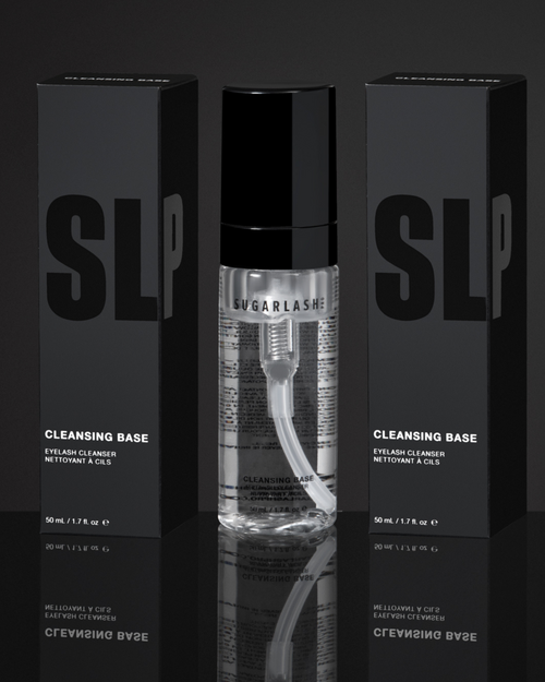 A cleansing base bottle in between two packaged bottles of the product for eyelash extensions.