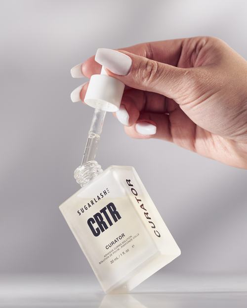 A model taking the eyelash extension solution "Curator"dropper out of the bottle.