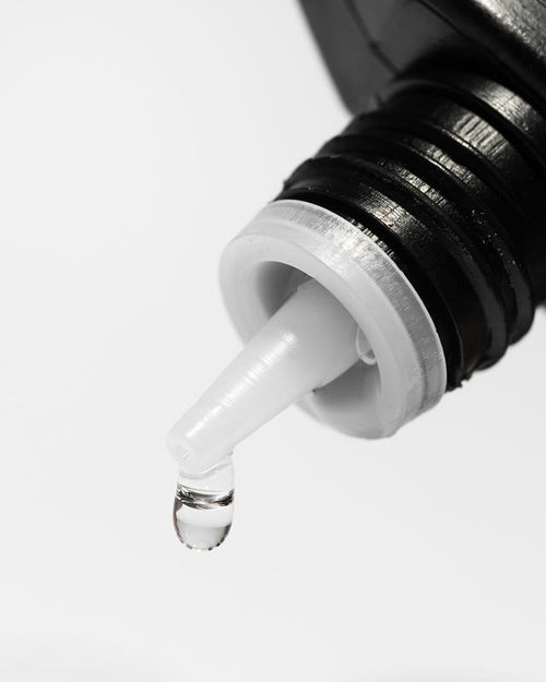 A drop coming out of a bottle of Naked Bond eyelash glue for extensions.