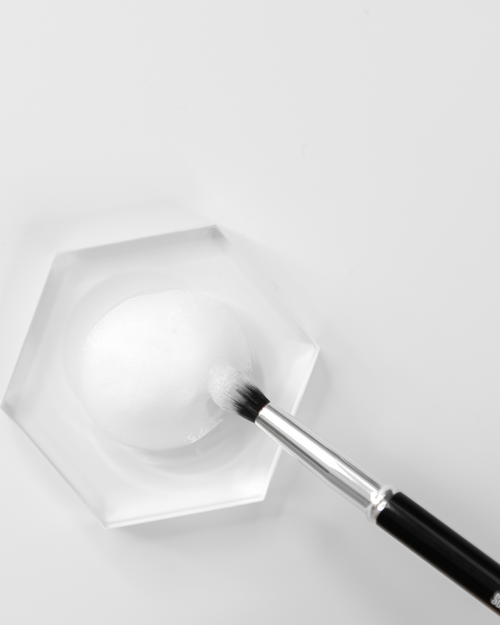 A Lash Extensions Brush dipping into a small tile holding foaming cleanser.