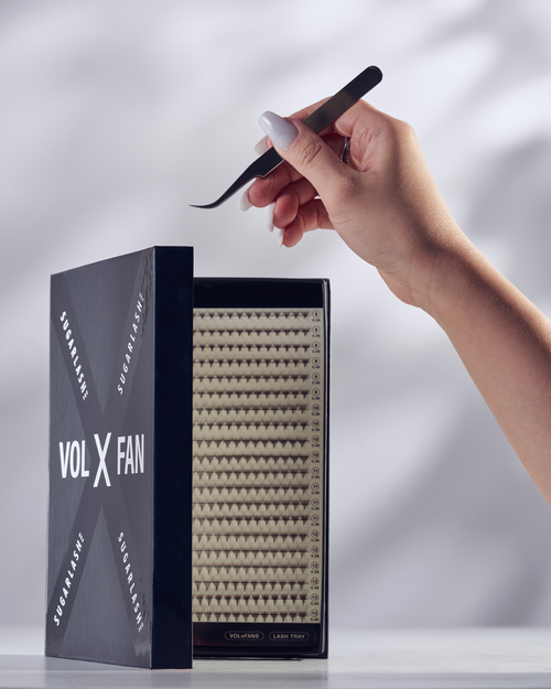 A model holding tweezers over a partially open tray of VOL-X Pre-made Fans, eyelash extensions